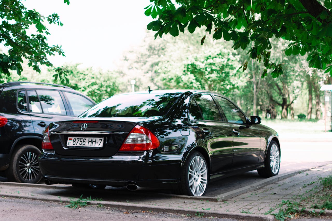 A sleek black car parked in an outdoor lot under lush green trees on a sunny day.