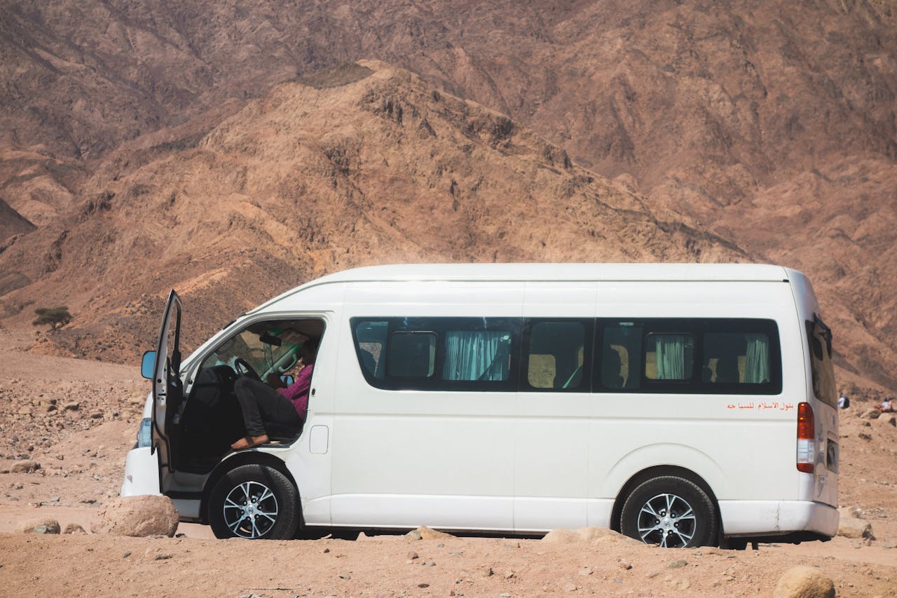 A white van parked in a desert setting with rocky hills in the background, perfect for travel themes.