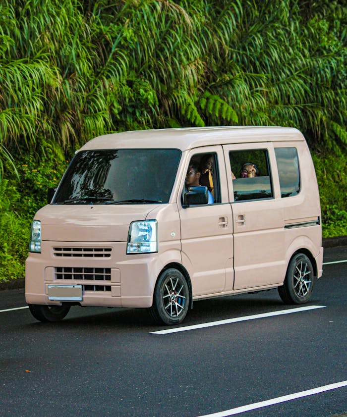 Pink van driving on a lush green road, ideal for travel and transportation themes.