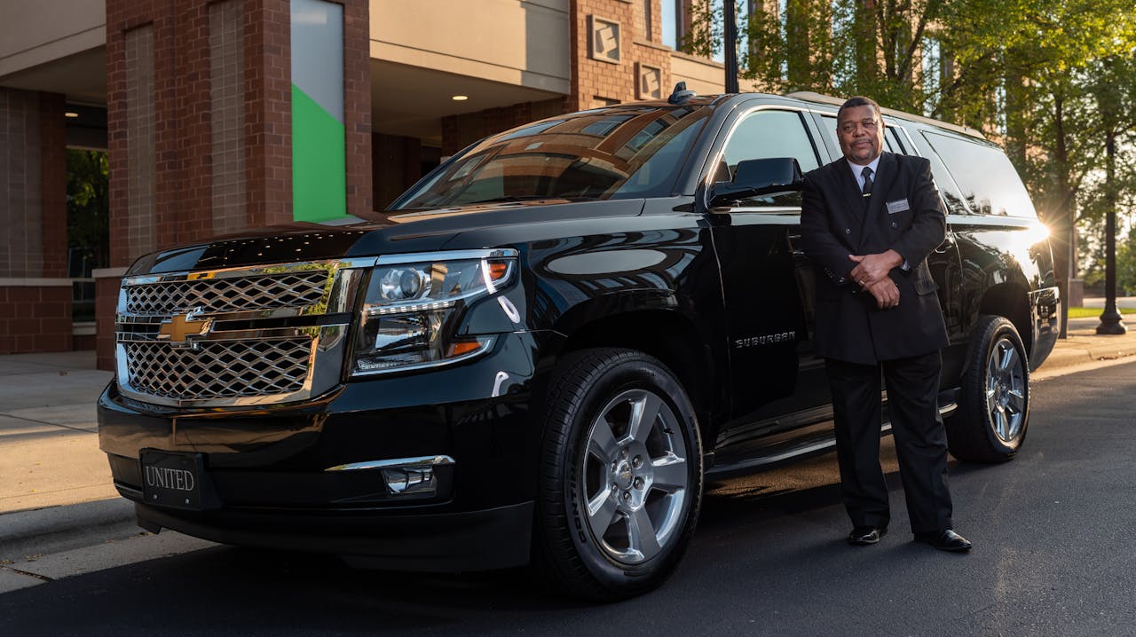Chauffeur standing confidently next to a black SUV, offering luxury transportation service.